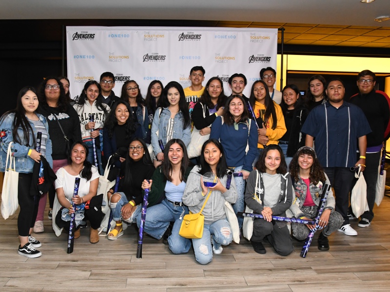 Large group of people in front of a step-and-repeat sign with The Solutions Project and Avengers logos on it
